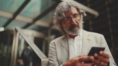 Gözlüklü, sakallı, olgun bir iş adamı iş merkezinin arka planında caddede duruyor. Orta yaşlı bir yönetici akıllı telefona mesaj yolluyor. Üzüntü iyi bir anlaşma değil.