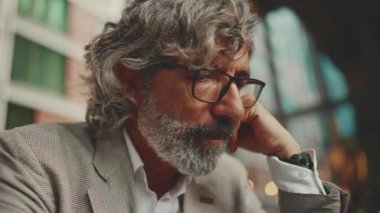 Clouse up, mature businessman with beard in eyeglasses,wearing gray jacket is working using tablet