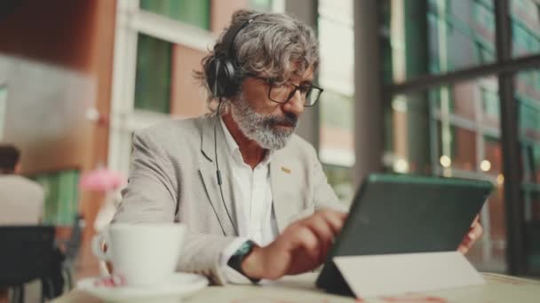 Mature Businessman Beard Eyeglasses Headphones Sits Outdoor Cafe Works Using — 图库视频影像