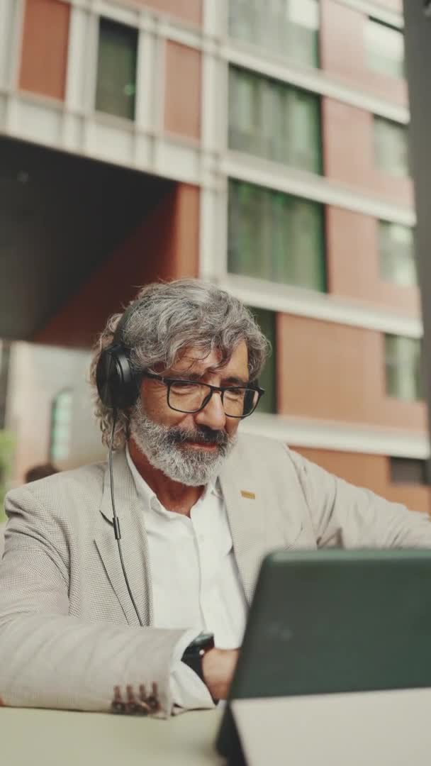 Vertical Video Mature Businessman Beard Eyeglasses Headphones Sits Outdoor Cafe — Wideo stockowe