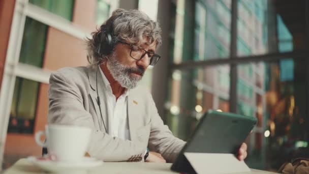 Mature Businessman Beard Eyeglasses Headphones Sits Outdoor Cafe Works Using — 图库视频影像