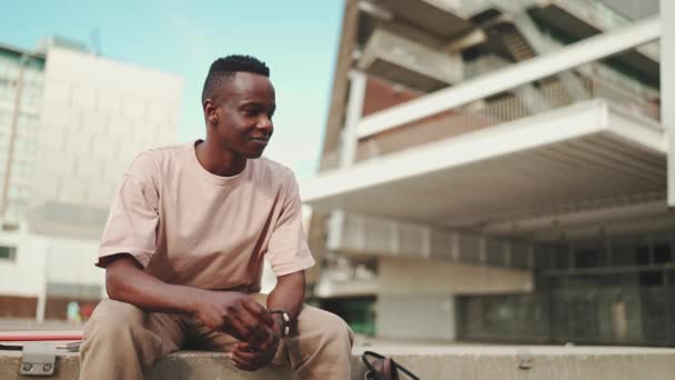 Усміхнений Молодий Африканський Студент Сидить Межами Університету Дивлячись Навколо — стокове відео