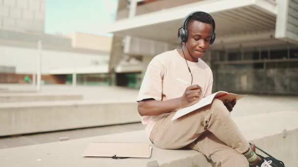 Mladý Africký Student Sedí Mimo Univerzitu Dělá Poznámky Při Poslechu — Stock video