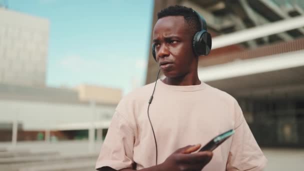 Young African Student Sitting University Wearing Headphones Using Phone Listening — ストック動画
