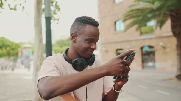 Smiling Young African Student Sits Bench University Headphones Uses Phone — Stock video