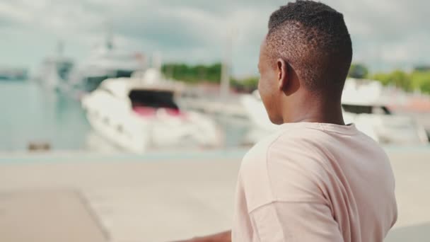 Young African Guy Sits Looks Yachts Ships Embankment — Vídeo de Stock