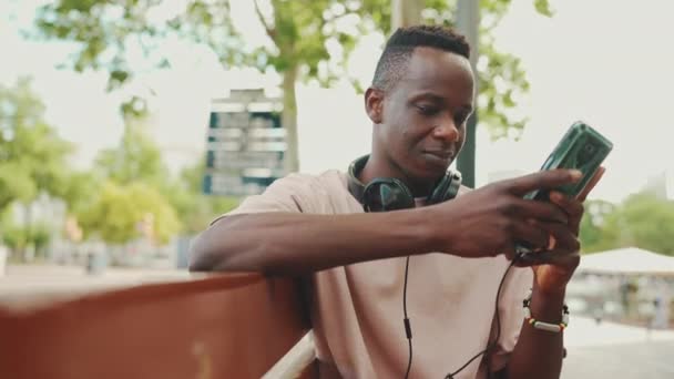 Mladý Africký Student Sedí Lavičce Mimo Univerzitu Sluchátkách Používá Telefon — Stock video