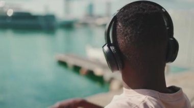Clouse yukarı, genç Afrikalı adam bankta oturup kulaklıkla müzik dinliyor.
