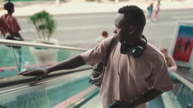 Young african guy in headphones uses the escalator, rises