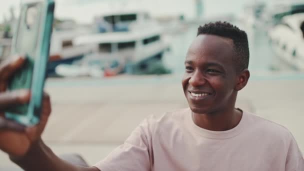 Smiling Young African Guy Uses Phone While Standing Embankment Yachts — Stock video