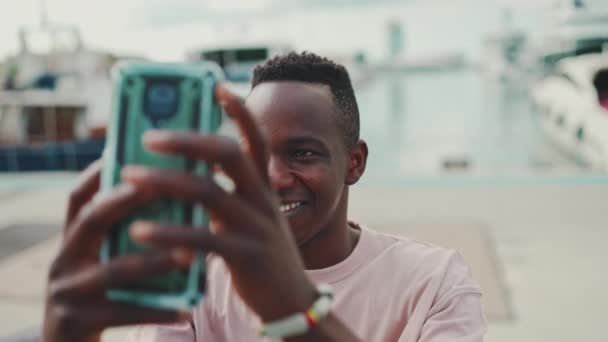 Усміхнений Молодий Африканський Хлопець Використовує Телефон Стоячи Набережній Яхтами Кораблями — стокове відео