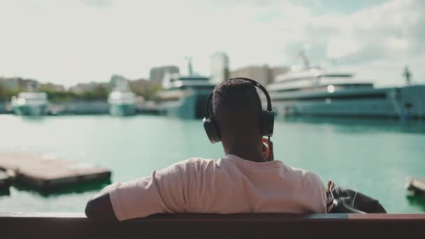 Young African Guy Relaxes Sitting Bench Port Listens Music Headphones — Vídeo de Stock