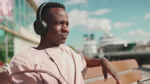 Young African Guy Relaxes Sitting Bench Port Listens Music Headphones — Stock video