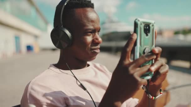 Young African Guy Relaxes Sitting Bench Port Listens Music Headphones — Vídeo de Stock