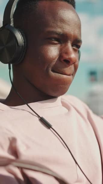Vertical Video Usmívající Mladý Afričan Odpočívá Lavičce Přístavu Poslouchá Hudbu — Stock video