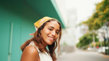 Uzun kahverengi saçlı, beyaz bluzlu, sarı bandanalı hoş bir kadın kablosuz kulaklıkla müzik dinliyor ve mavi duvar arkasında dans ediyor.. 