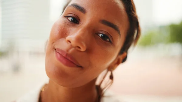 Close-up of the face of beautiful tanned woman with dark hair and expressive brown eyes looks at the camera with smile