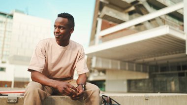 Smiling young african student sitting outside of university, looking around