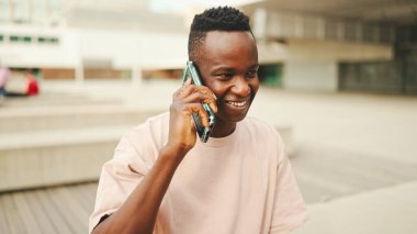 Üniversitenin dışında oturan gülümseyen Afrikalı genç bir öğrenci cep telefonuyla konuşuyor.. 