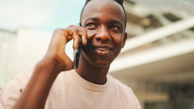 Üniversitenin dışında oturan gülümseyen Afrikalı genç bir öğrenci cep telefonuyla konuşuyor.. 