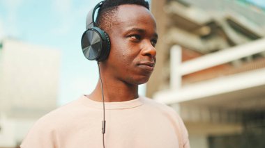 Üniversitenin dışında oturan genç Afrikalı öğrenci kulaklık takıyor.