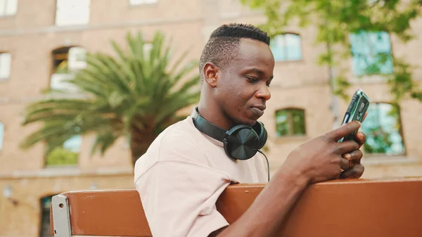 Smiling Young African Student Sits Bench University Headphones Uses Phone — Stockfoto