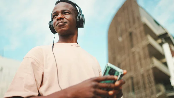 Young African Student Sitting University Wearing Headphones Using Phone Listening — Stockfoto