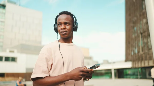 Young African Student Sitting University Wearing Headphones Using Phone Listening — Φωτογραφία Αρχείου