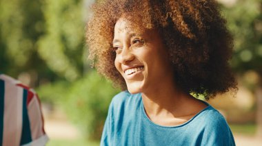 Kıvırcık saçlı, çizgili tişörtlü, parkta oturmuş, yaz günü dışarıda piknik yapan arkadaşlarıyla konuşan genç bir adam.