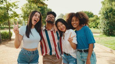 Happy, lovely multiethnic young people posing for the camera on summer day outdoors. group of friends hugging each other smiling at the camera while standing on path in the park