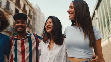 Mutlu çoklu etnik çeşitlilikte genç insanlar yaz günü açık havada kucaklaşarak yürürler. Bir grup arkadaş sokakta yürürken neşeyle konuşuyor ve gülüyorlar.