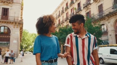 Young multiethnic couple walk laughing down the street on warm summer day, meeting friends, enjoy meeting and hugging