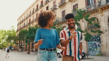 Genç çok ırklı çift sıcak bir yaz günü sokakta gülerek, arkadaşlarıyla tanışarak, tanışarak ve kucaklaşarak yürüyor.