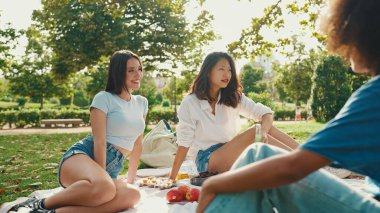 Yaz günü açık havada piknikte gülümseyen mutlu çokuluslu genç insanlar. Arkadaşlar hafta sonu eğleniyor, piknikte parkta dinleniyorlar.