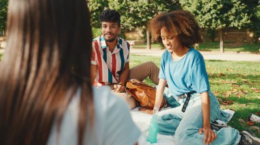 Yaz günü açık havada piknikte gülümseyen mutlu çokuluslu genç insanlar. Arkadaşlar hafta sonu eğleniyor, piknikte parkta dinleniyorlar.