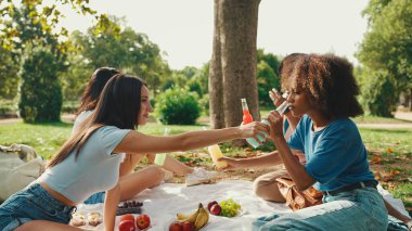 Happy smiling young multinational people at picnic on summer day outdoors. Friends have fun weekend together, relaxing in the park at picnic