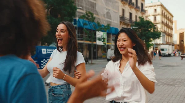 Young multiethnic women walk laughing down the street on warm summer day, meeting couple friends, enjoy meeting and hugging