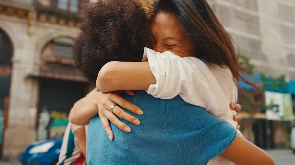 Young multiethnic couple walk laughing down the street on warm summer day, meeting friends, enjoy meeting and hugging