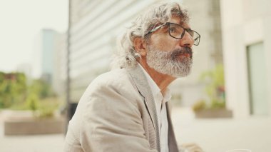 Gözlüklü, sakallı, gri ceketli, olgun iş adamı. Etrafına bir bak.