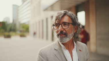 Gözlüklü, gri ceketli, sakallı, olgun bir işadamı gibi modern binaların önünden geçeceğiz.