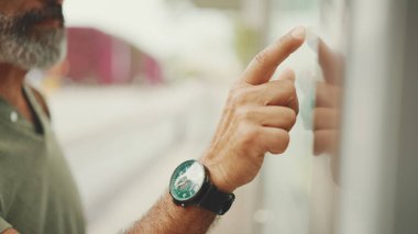 Gri saçlı ve sakallı orta yaşlı adam profili, kentin ulaşım çizelgesinde parmaklarını gezdiriyor. Gözlüklü beyefendi tramvayı bekliyor.