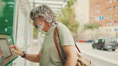 Gri saçlı ve sakallı arkadaş canlısı orta yaşlı bir adam toplu taşıma için bilet alır. Omzunda çanta olan gözlüklü bir beyefendi bilet alır.