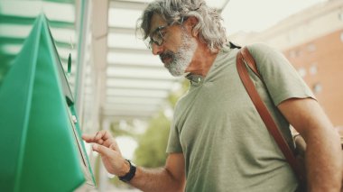 Gri saçlı ve sakallı arkadaş canlısı orta yaşlı bir adam toplu taşıma için bilet alır. Omzunda çanta olan gözlüklü bir beyefendi bilet alır.