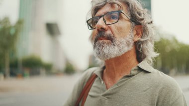 Clouse-up, friendly middle-aged man with gray hair and beard wearing casual clothes 