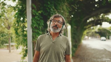 Dost canlısı, orta yaşlı, gri saçlı, sakallı sıradan kıyafetler giyen kulaklıkla müzik dinleyen bir adam. Gözlüklü, olgun bir beyefendi açık havada müzik dinlemekten hoşlanır.