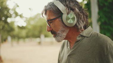 Dost canlısı, orta yaşlı, gri saçlı, sakallı sıradan kıyafetler giyen kulaklıkla müzik dinleyen bir adam. Gözlüklü, olgun bir beyefendi açık havada müzik dinlemekten hoşlanır.