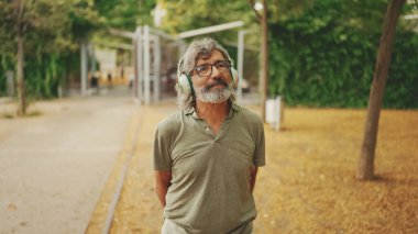 Dost canlısı, orta yaşlı, gri saçlı, sakallı sıradan kıyafetler giyen kulaklıkla müzik dinleyen bir adam. Gözlüklü, olgun bir beyefendi açık havada müzik dinlemekten hoşlanır.