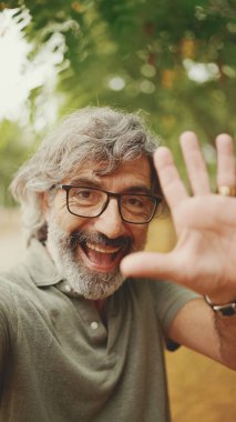 Gri saçlı, sakallı, sıradan kıyafetler giyen orta yaşlı arkadaş cep telefonu kullanıyor. Gözlüklü olgun bir beyefendi cep telefonuyla fotoğraf çeker.