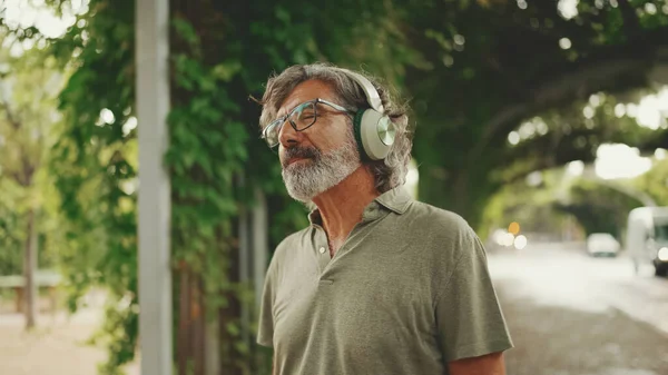 머리에 턱수염을 남자가 헤드폰으로 음악을 안경을 밖에서 음악을 즐긴다 — 스톡 사진