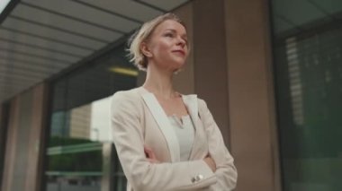 Smiling woman with blond hair wearing beige suit walks down the street and looks around